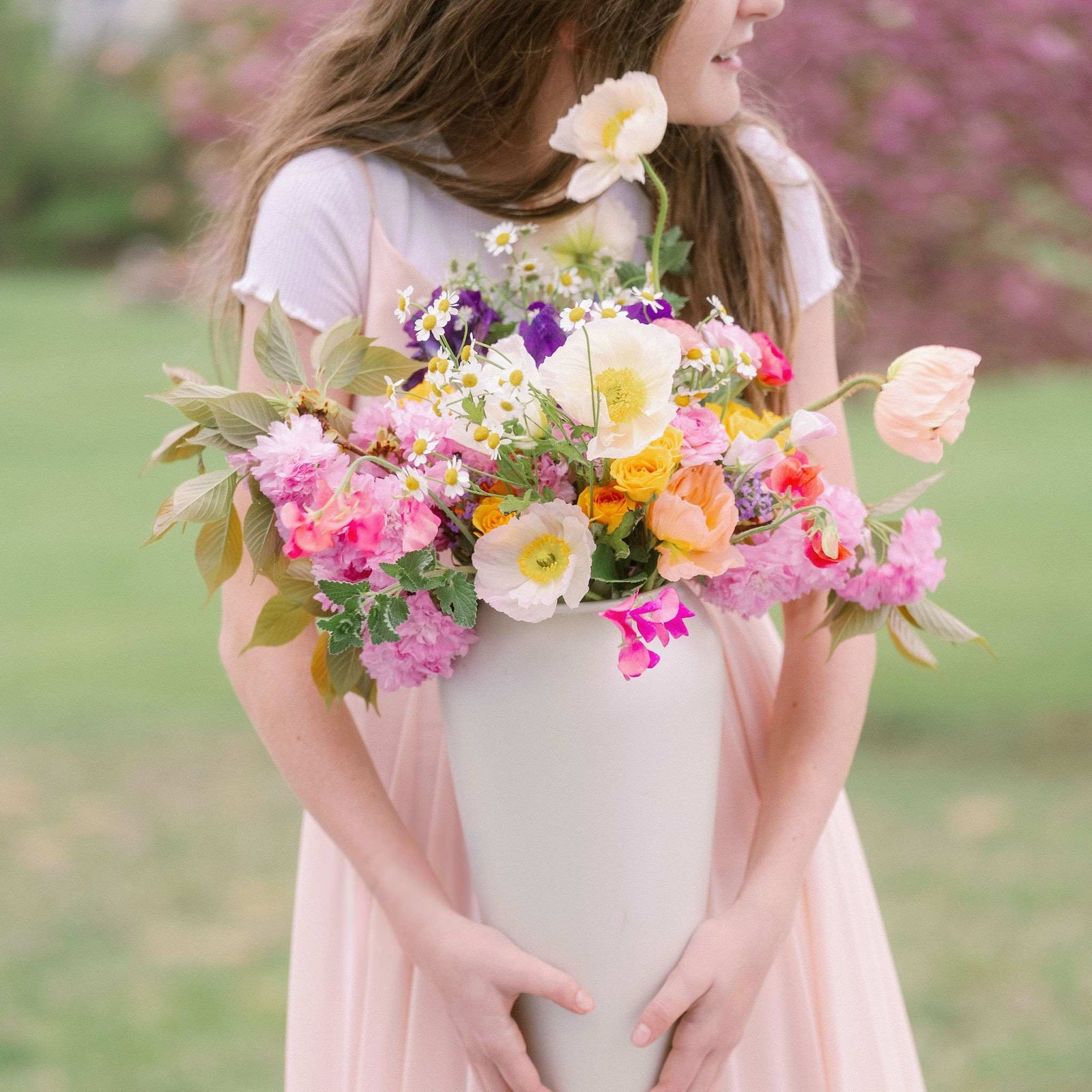 Young girl holding classic white vase with spring floral arrangment